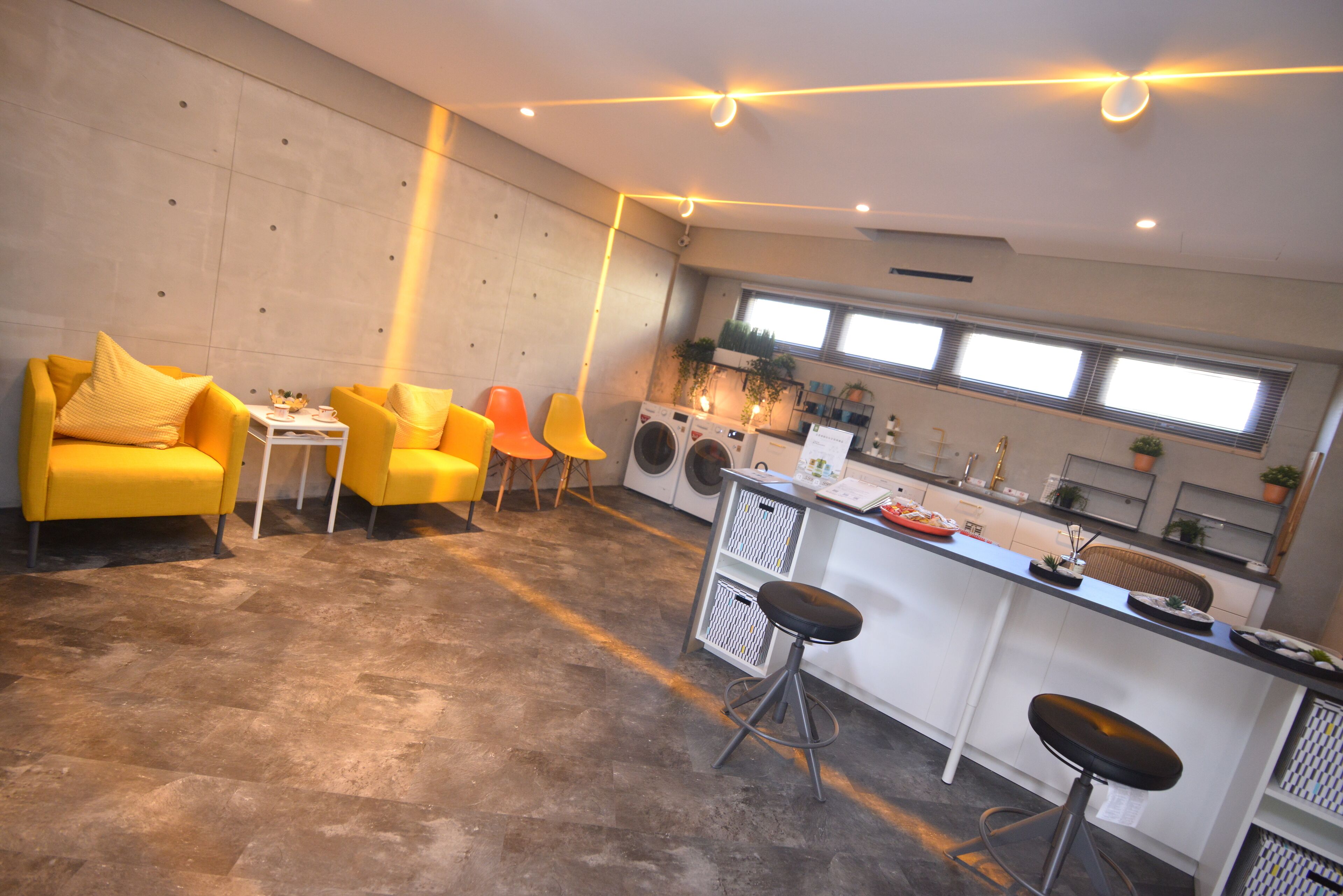 A modern kitchen with a bar area, yellow chairs, and a washing machine.