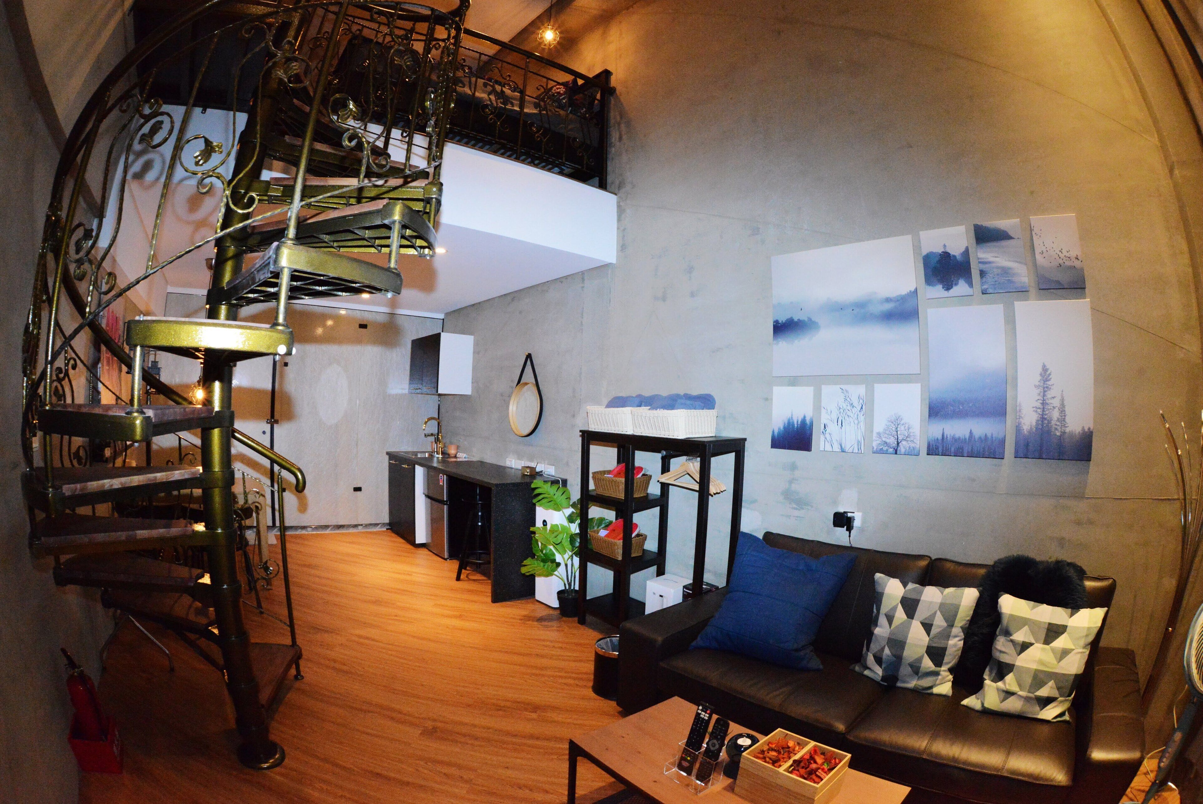 A modern living space with a spiral staircase, a sofa with patterned cushions, a small table, and a wall with framed pictures.