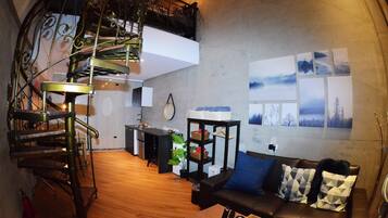 A modern living space with a spiral staircase, a sofa with patterned cushions, a small table, and a wall with framed pictures.