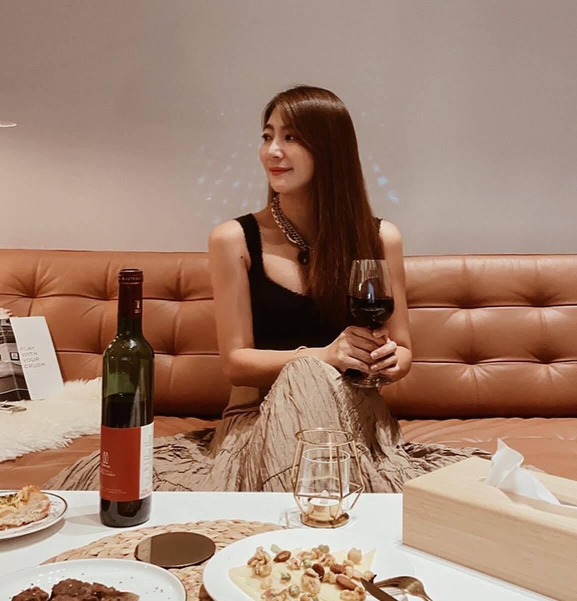 A person seated on a brown leather couch with a bottle of wine and a glass on a table in front of them.