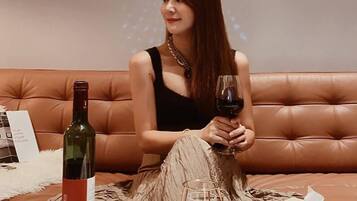 A person seated on a brown leather couch with a bottle of wine and a glass on a table in front of them.