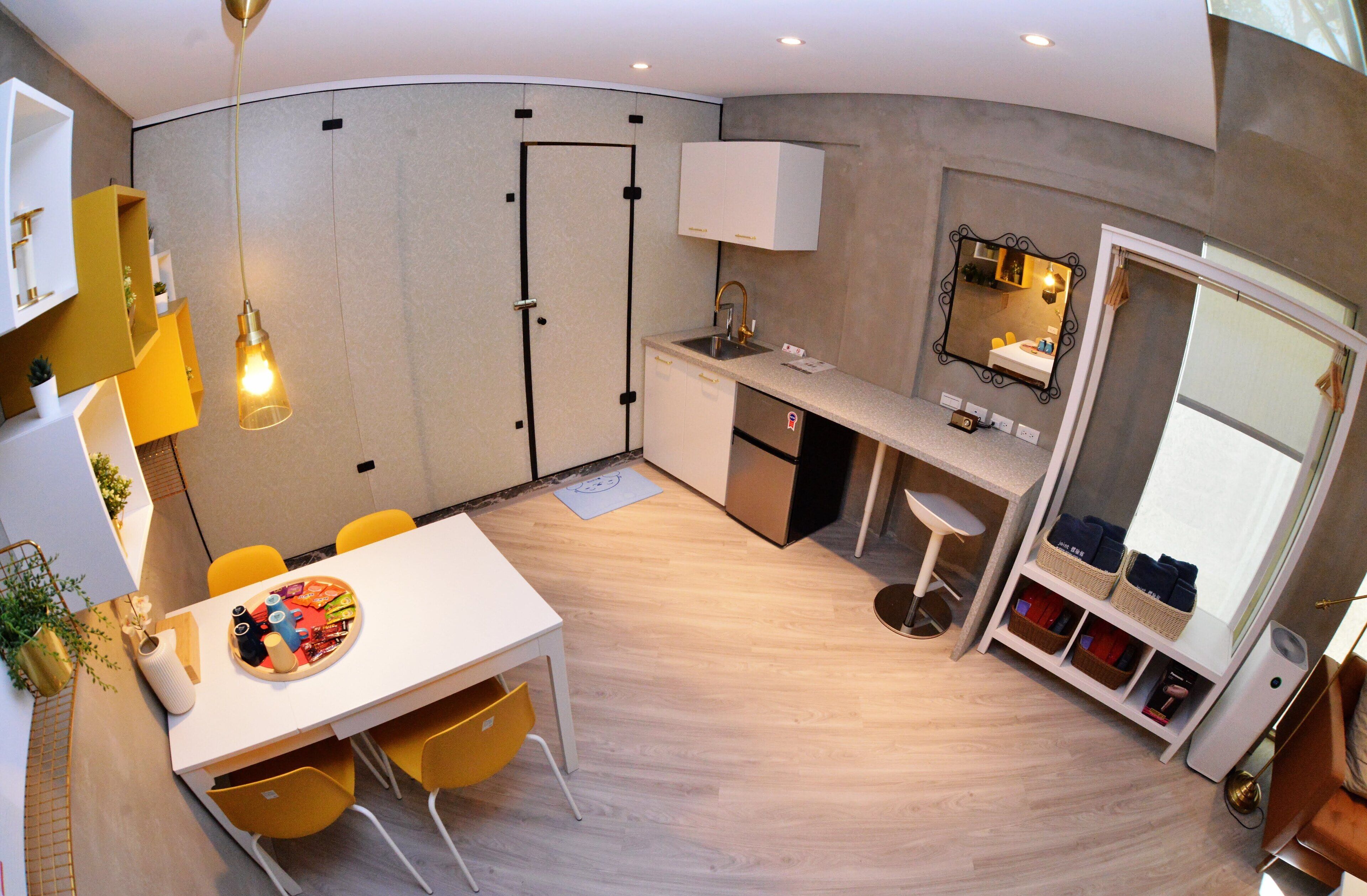 A compact kitchen with a sink, countertop, and a mirror. There is a dining area with a table and chairs.