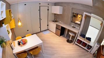 A compact kitchen with a sink, countertop, and a mirror. There is a dining area with a table and chairs.