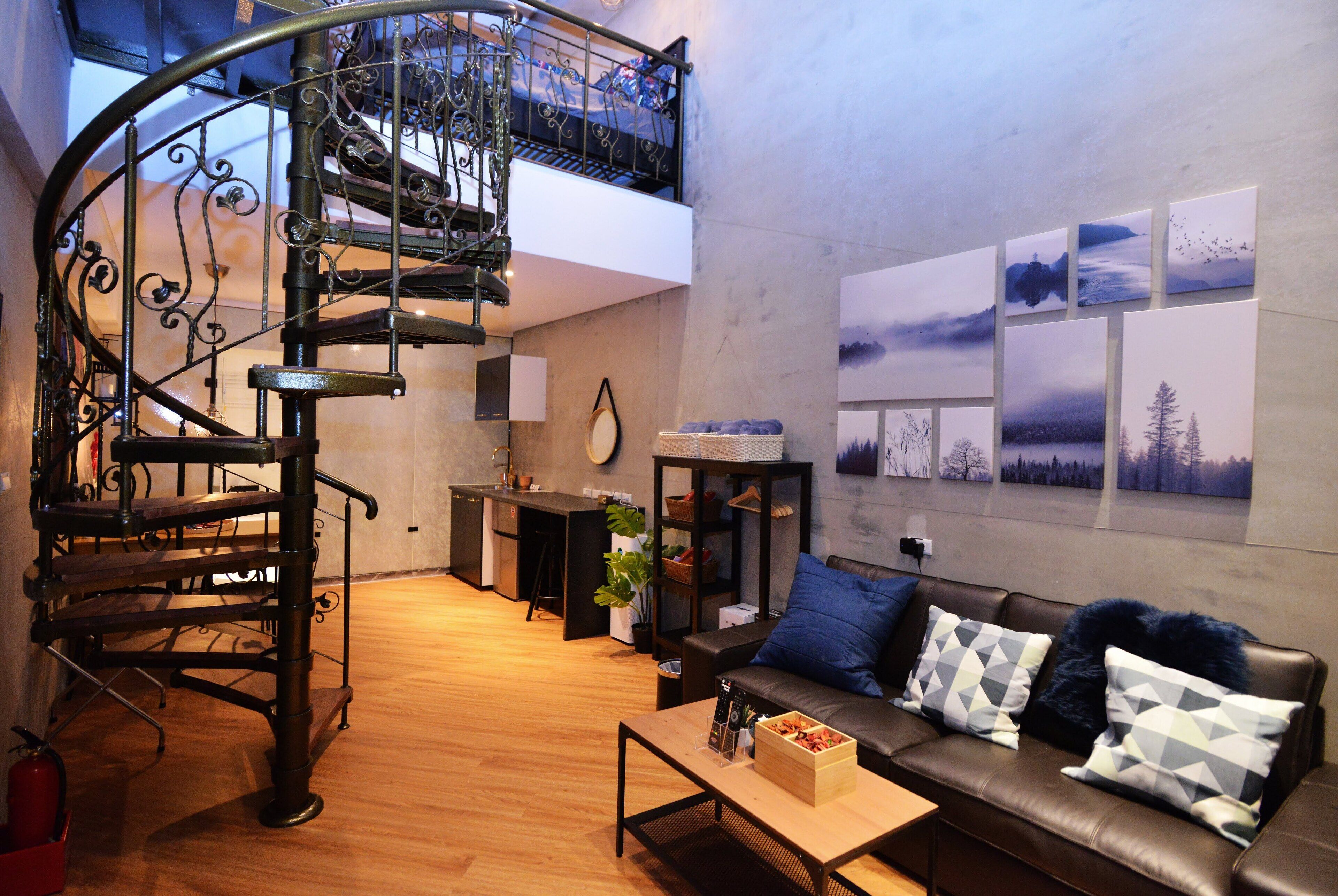 A modern living room with a curved staircase, a sofa with patterned cushions, a coffee table, and a wall with framed pictures.