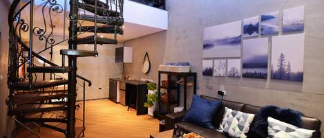 A modern living room with a curved staircase, a sofa with patterned cushions, a coffee table, and a wall with framed pictures.