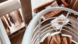Eine Wendeltreppe mit Holzverkleidung und weißen Geländern führt zu einer Sitzgruppe mit einem braunen Ledersofa und gemusterten Kissen.