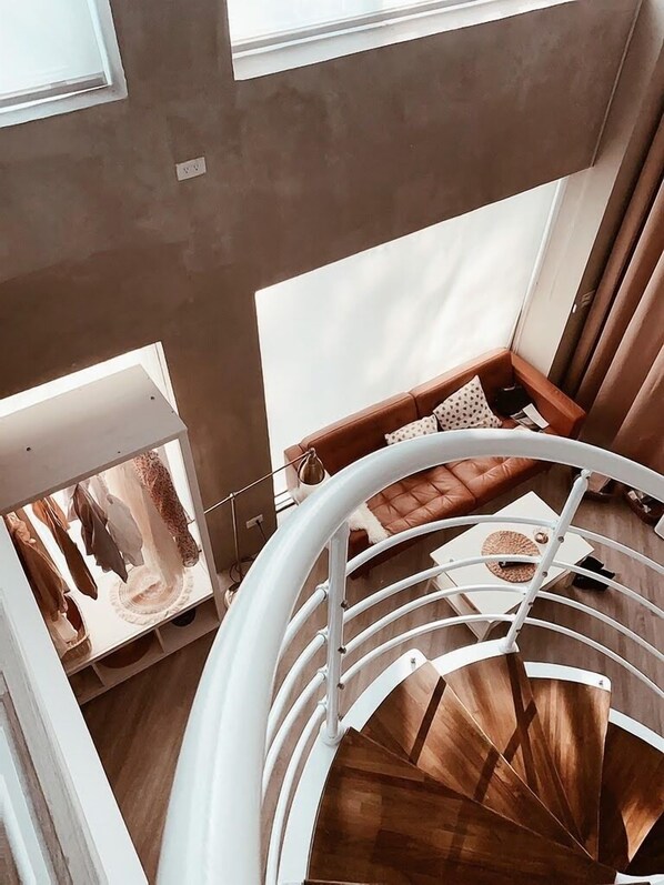 Una escalera de caracol con acabado de madera y barandillas blancas, que conduce a una zona de estar con un sofá de cuero marrón y cojines estampados.
