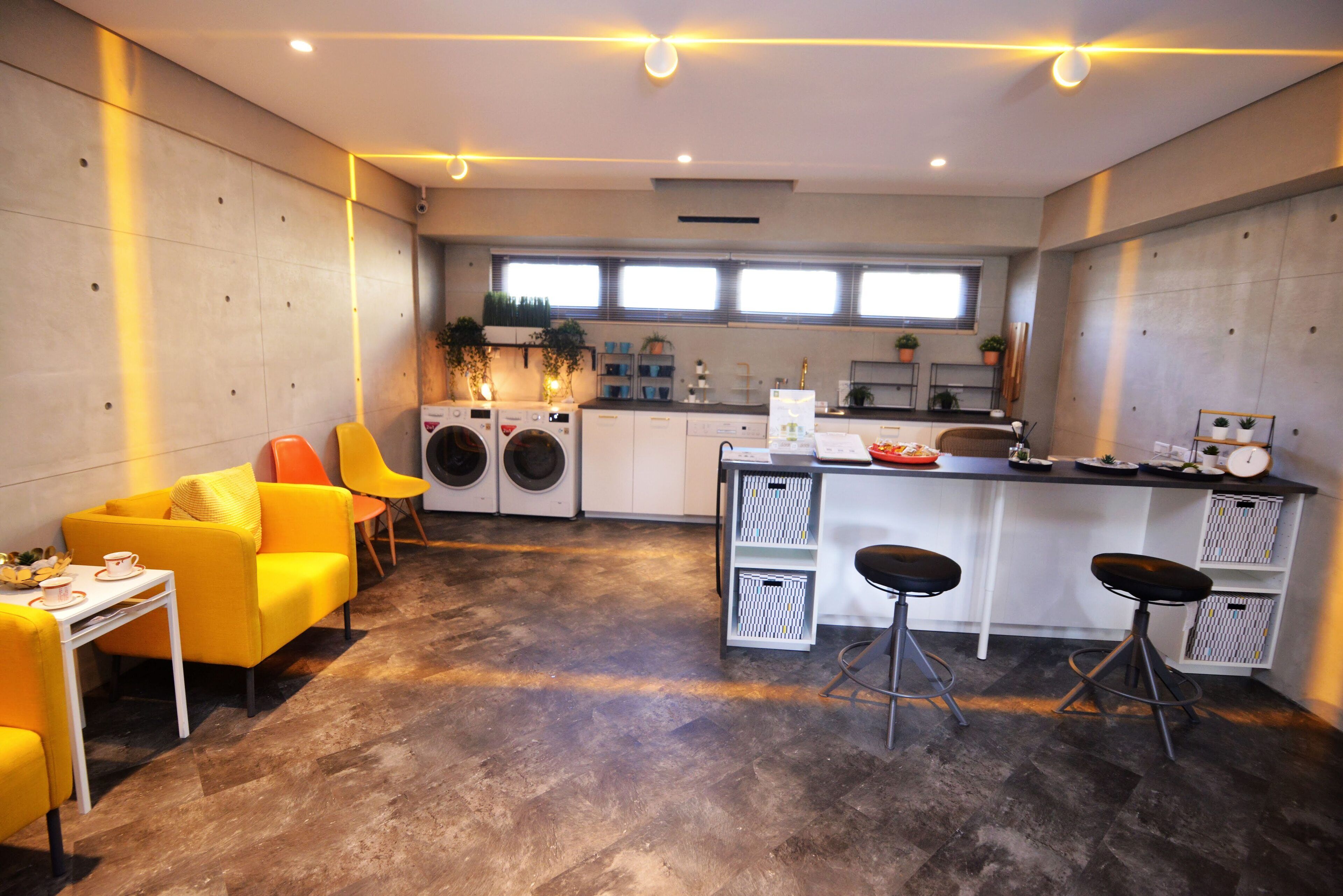 A modern kitchen with a bar area, a washing machine, and a dining area with yellow chairs.