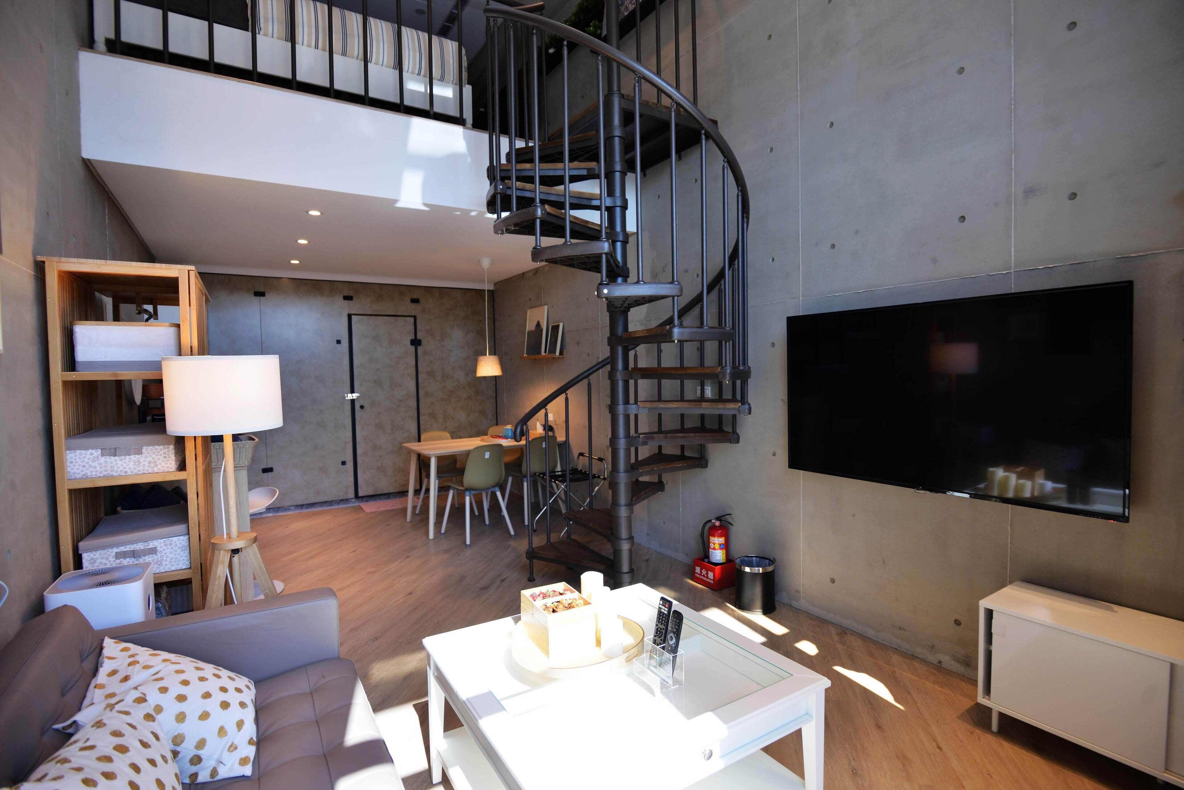 A modern living room with a spiral staircase, a flat-screen TV, a sofa, a coffee table, and a dining area.