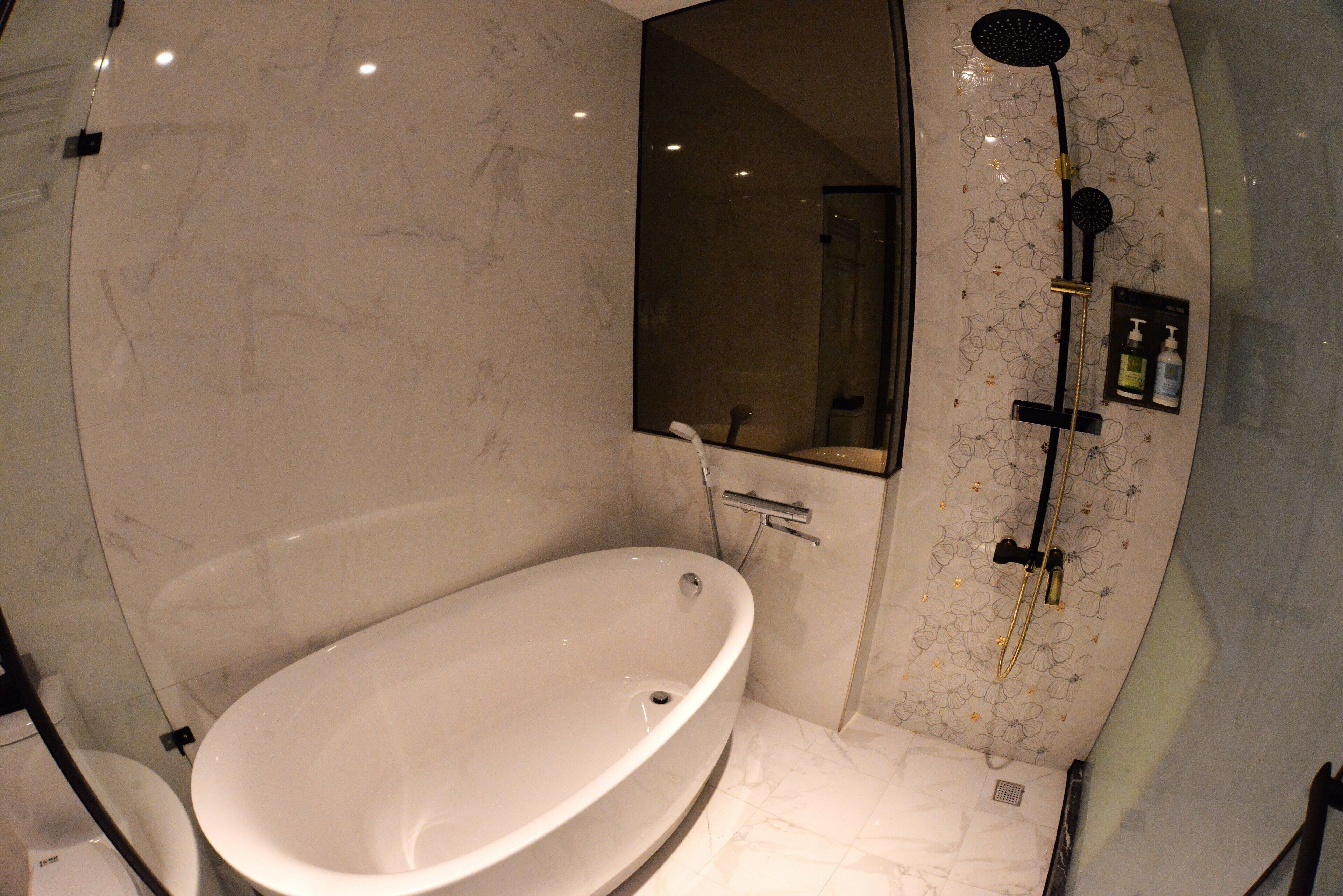 A bathroom with a large oval bathtub, a shower with a floral pattern, and a mirror.