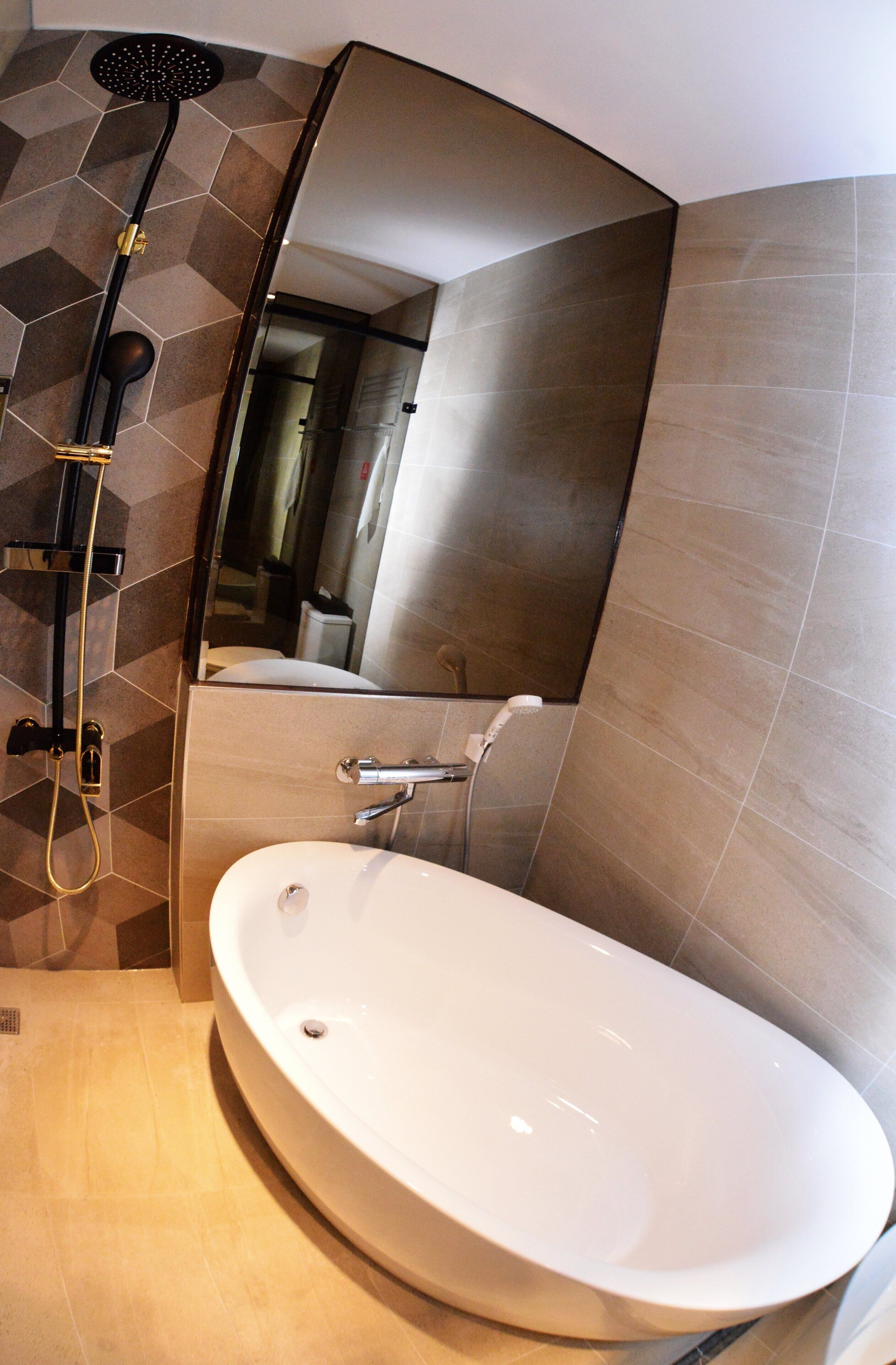A modern bathroom with a freestanding bathtub, a showerhead, and a large mirror.