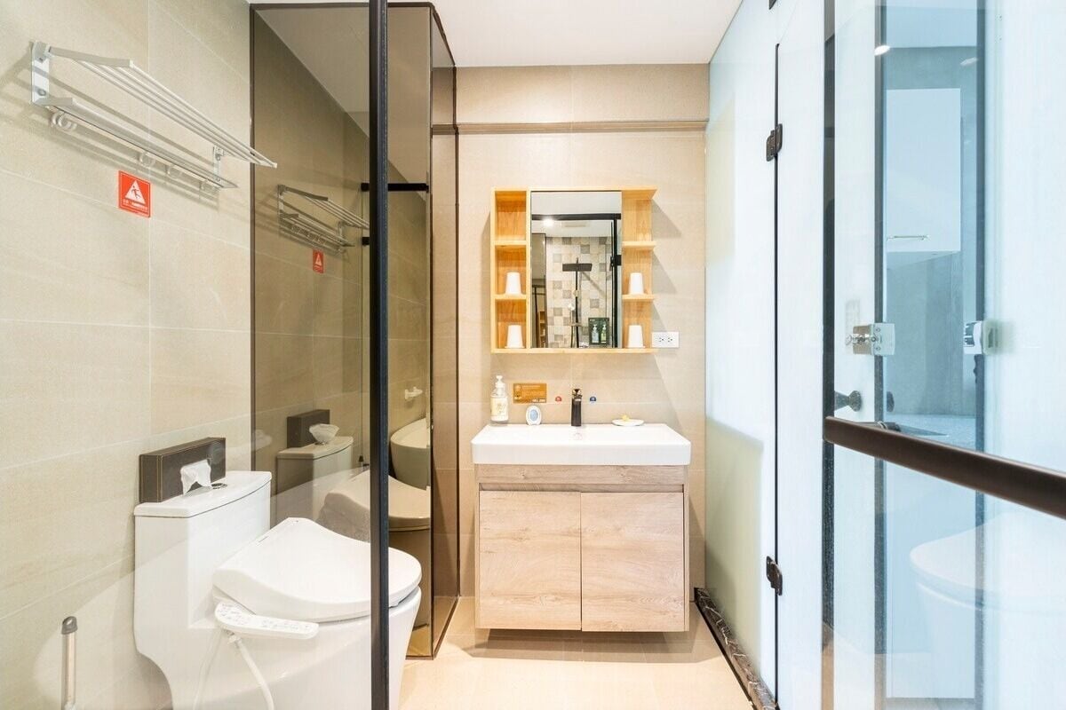 A modern bathroom with a glass shower enclosure, a toilet, a sink with a wooden vanity, and a mirror with shelves.