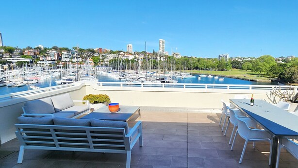 Une terrasse avec des places assises extérieures et une vue sur un port de plaisance rempli de bateaux.