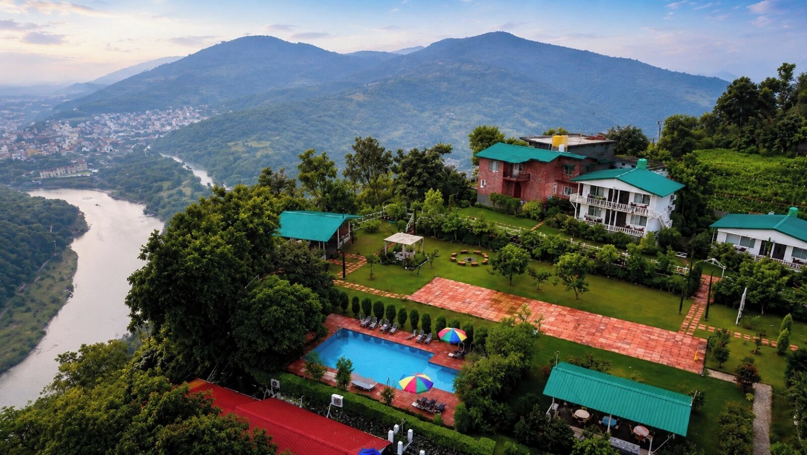 A resort with a swimming pool, lush greenery, and a river in the background.