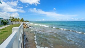 A beachfront property with a white fence, a grassy area, and a view of the ocean.