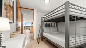 A bunk bed room with a desk and chair, a ladder, and a door leading to another room.
