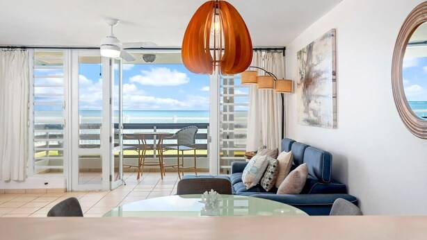 A modern living room with a balcony, a ceiling fan, and a view of the ocean.