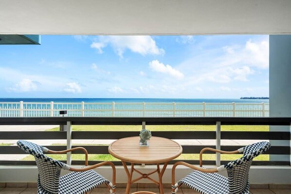 Un balcon avec vue sur la mer, deux fauteuils en osier et une petite table ronde.