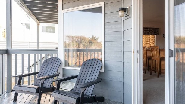 Una terraza de madera con dos sillas Adirondack y una puerta corrediza de vidrio que da a un comedor interior.