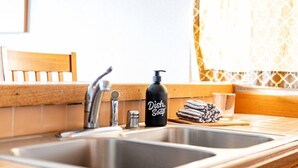 Un lavamanos de cocina con una botella de detergente para platos negro, un vaso y una toalla sobre la encimera.