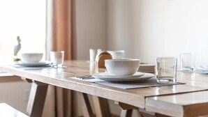 Una mesa de comedor con vajilla y copas blancas, una mesa de madera y un cuadro en la pared.