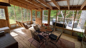 Eine Holzterrasse mit Tisch und Stühlen, einer hängenden Lampe und Blick auf die umliegenden Bäume.