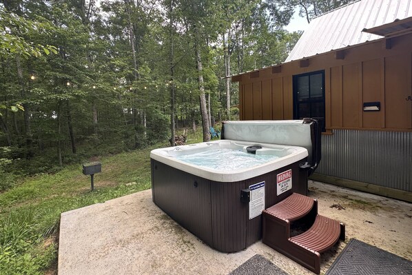 Un bain à remous situé dans un espace boisé, avec un chalet en bois en arrière-plan.
