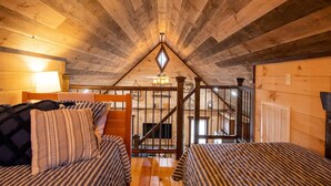 Ein gemütliches Schlafzimmer im Dachgeschoss mit Holzbalken, einer Treppe und zwei Betten mit gestreifter Bettwäsche.