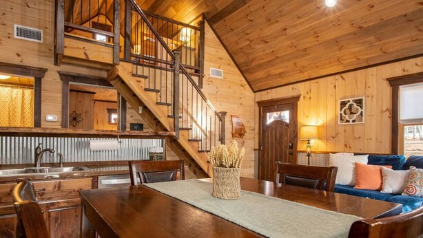 Ein Holzinnenraum mit einem Esstisch, Stühlen, einer Treppe und einem Sofa.