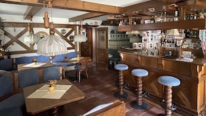 Un interior rústic amb bigues de fusta, una zona de bar amb tamborets i una zona de menjador amb cadires blaus i taules.
