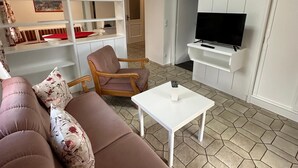 Un saló modern amb un sofà, una cadira, una taula baixa, una televisió i prestatgeries integrades.