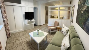 En moderne stue med en grøn sofa, et hvidt sofabord og et fjernsyn på et hvidt skab.