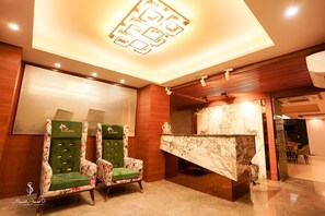 A hotel lobby with two green upholstered chairs, a marble reception desk, and a ceiling light fixture. - The Olivia (Varanasi)