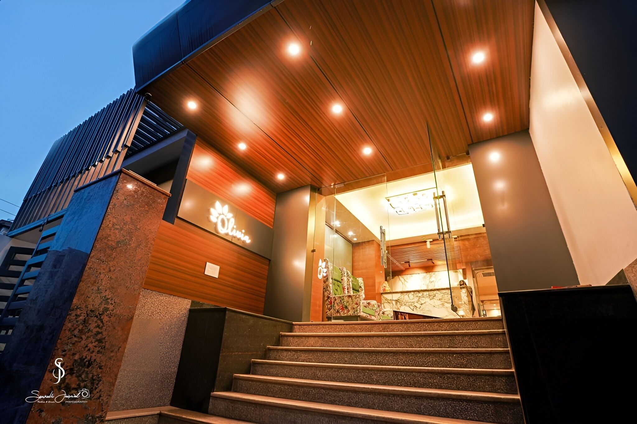 Entrada de hotel moderna con fachada de madera, una escalera que conduce a la recepción y un letrero con el nombre 'Olive'.