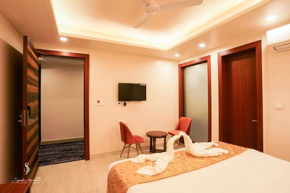 A hotel room with a bed, a TV, a desk with a chair, and a red chair.