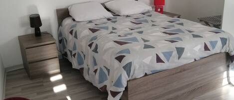 Un dormitorio con cama, mesita de noche, una silla roja y un adorno en la pared.