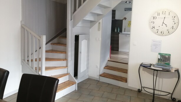 A staircase leading to a second floor, a dining area with chairs, a clock, and a small table with books. - ENTRE MER ET FORET" vacation home (Le Tréport)