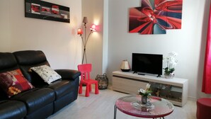 A modern living room with a black leather sofa, a red chair, a glass coffee table, a flat-screen TV, and a large abstract painting on the wall. - ENTRE MER ET FORET" vacation home (Le Tréport)
