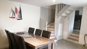 A dining area with a wooden table and black chairs, a staircase, and a wall-mounted sailboat decoration. - ENTRE MER ET FORET" vacation home (Le Tréport)