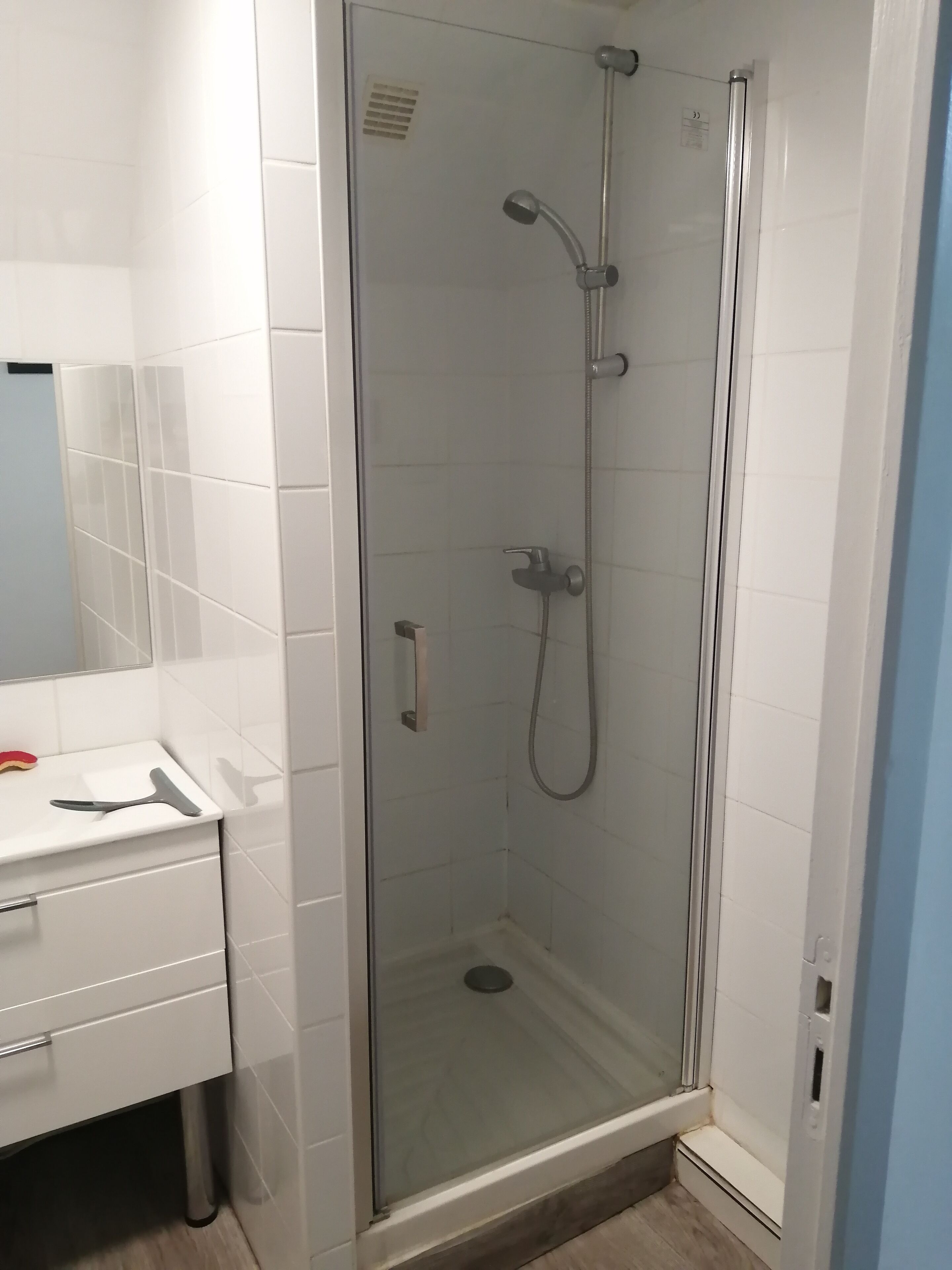 Ducha con mampara de vidrio, cabezal de ducha de mano y grifo empotrado en la pared.