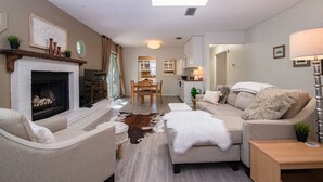 Un salon avec une cheminée, un canapé, une table basse et un coin repas comprenant une table et des chaises.