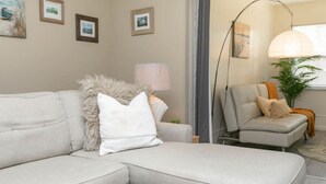 Un salon avec un canapé gris, un coussin blanc, une lampe sur pied et une table d’appoint.