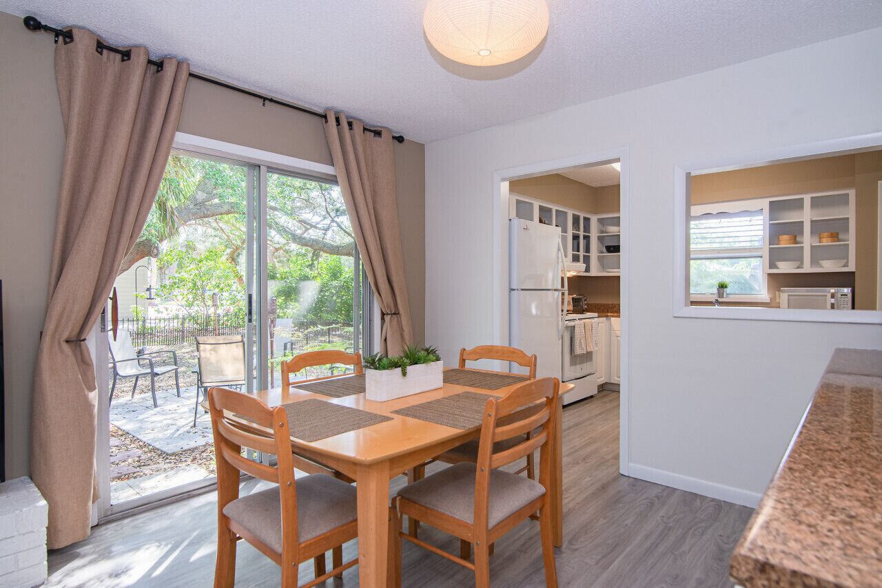 A dining area with a wooden table and chairs, a window with curtains, and a view of the outdoors.