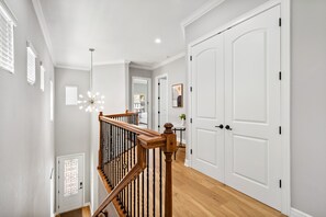 Un pasillo con una escalera de madera, puertas blancas y un candelabro en el techo.