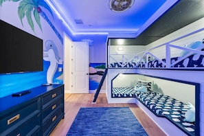 Un dormitorio con televisor, cama con colcha estampada, escalera con barandilla y un mural en la pared.