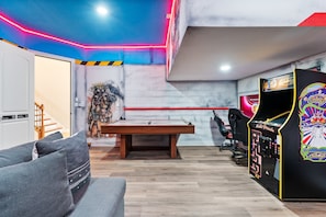 Una habitación con mesa de billar, sofá y máquina de videojuegos.