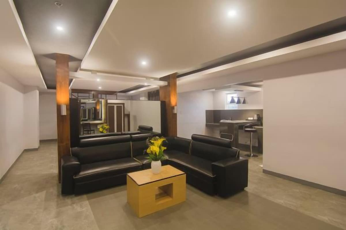 Un salón moderno con un sofá de cuero negro, una mesa de centro de madera y un jarrón con flores amarillas.