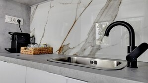 A kitchen with a modern design, featuring a marble backsplash, a stainless steel sink, and a black faucet. - Small & Chic Studio (Bucharest)