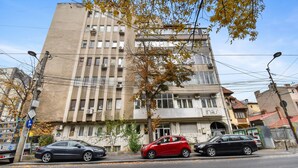 A multi-story building with a commercial ground floor, parked cars, and autumn leaves on the sidewalk. - Small & Chic Studio (Bucharest)