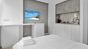 A modern bedroom with a bed, a TV mounted on the wall, and a built-in kitchen area with a marble backsplash. - Small & Chic Studio (Bucharest)